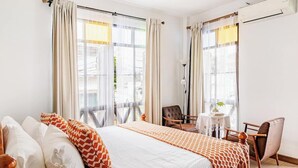 Ein Hotelzimmer mit einem großen Bett, zwei Stühlen, einem kleinen Tisch und einem fenster mit Vorhängen.