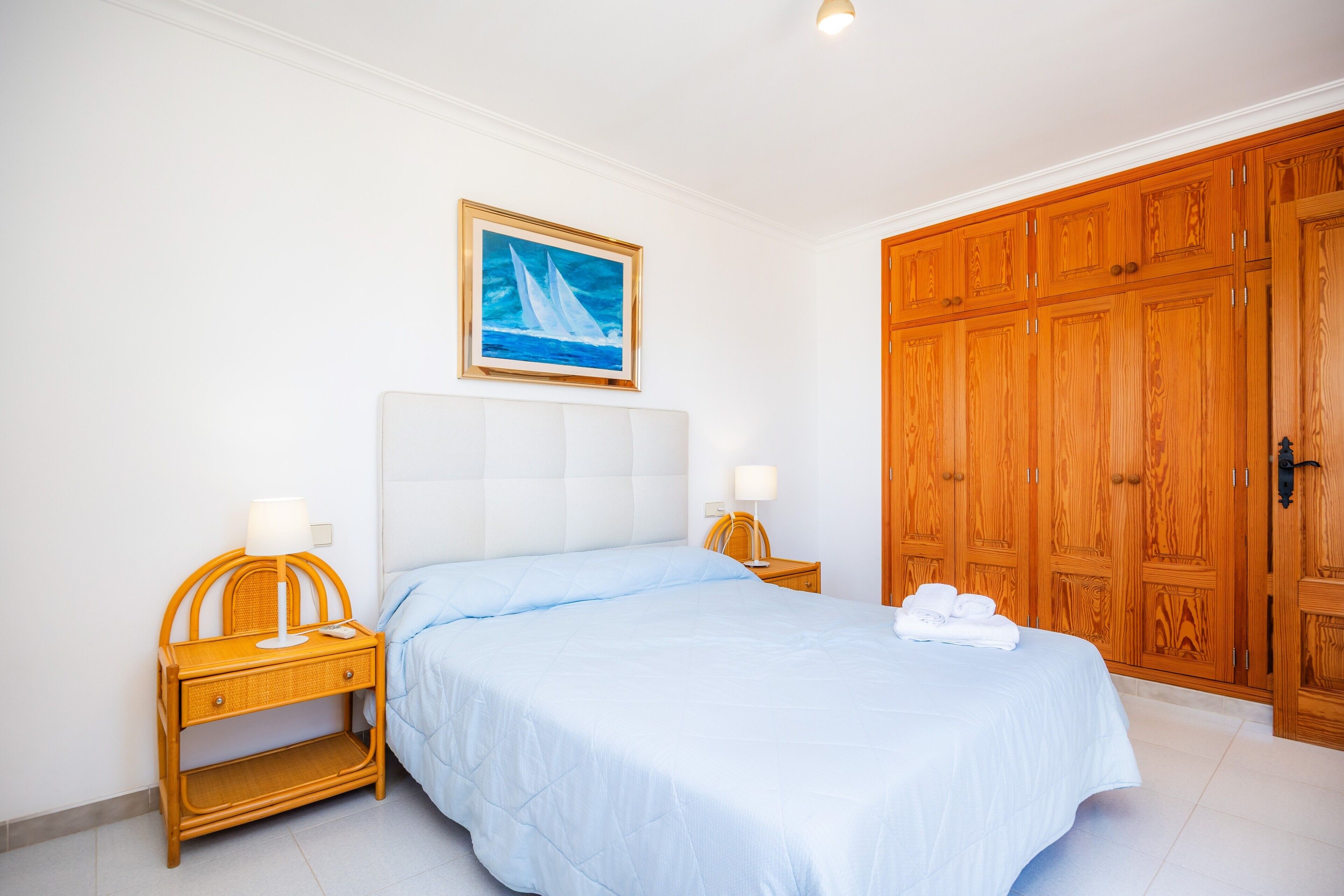 A bedroom with a bed, nightstands, a painting, and wooden wardrobe.