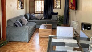 A living room with a grey sofa, a wooden coffee table, a glass table with papers, a TV, and a lamp. - Beautiful 2-bedroom apartment in Muyenga city center in Kampala with Lake View (Kampala)