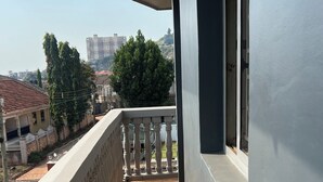 A balcony with a patterned floor, a railing, and a view of buildings and trees in the background. - Beautiful 2-bedroom apartment in Muyenga city center in Kampala with Lake View (Kampala)