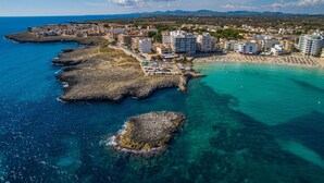 An aerial view of a coastal town with buildings along the shore, a beach, and rocky outcrops in the water.
