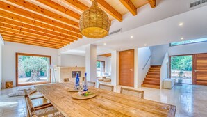 A spacious living area with a large wooden dining table, wicker chairs, and a hanging light fixture.