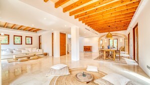 A spacious living area with a high wooden ceiling, a central round rug, and a dining area with a table and chairs.