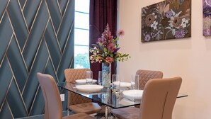 Un coin repas avec une table en verre, des chaises rembourrées et un vase rempli de fleurs.