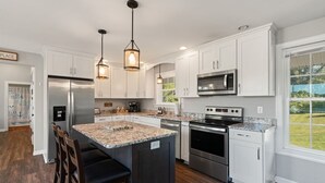 Une cuisine moderne avec des armoires blanches, des comptoirs en granit, des appareils en acier inoxydable et des luminaires suspendus.
