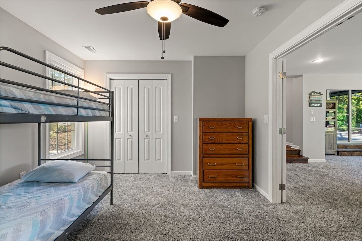 A bedroom with bunk beds, a ceiling fan, a wooden dresser, and a door leading to another room.