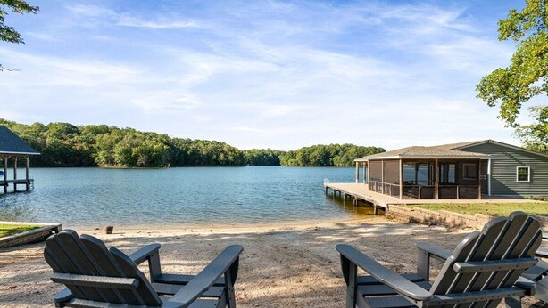Une vue sur le lac, avec un quai, un espace de détente abrité et une maison dotée d’une terrasse surplombant l’eau.