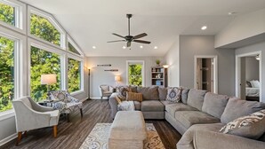 Un salon spacieux avec un grand canapé d’angle, un tapis à motifs et un ventilateur de plafond.