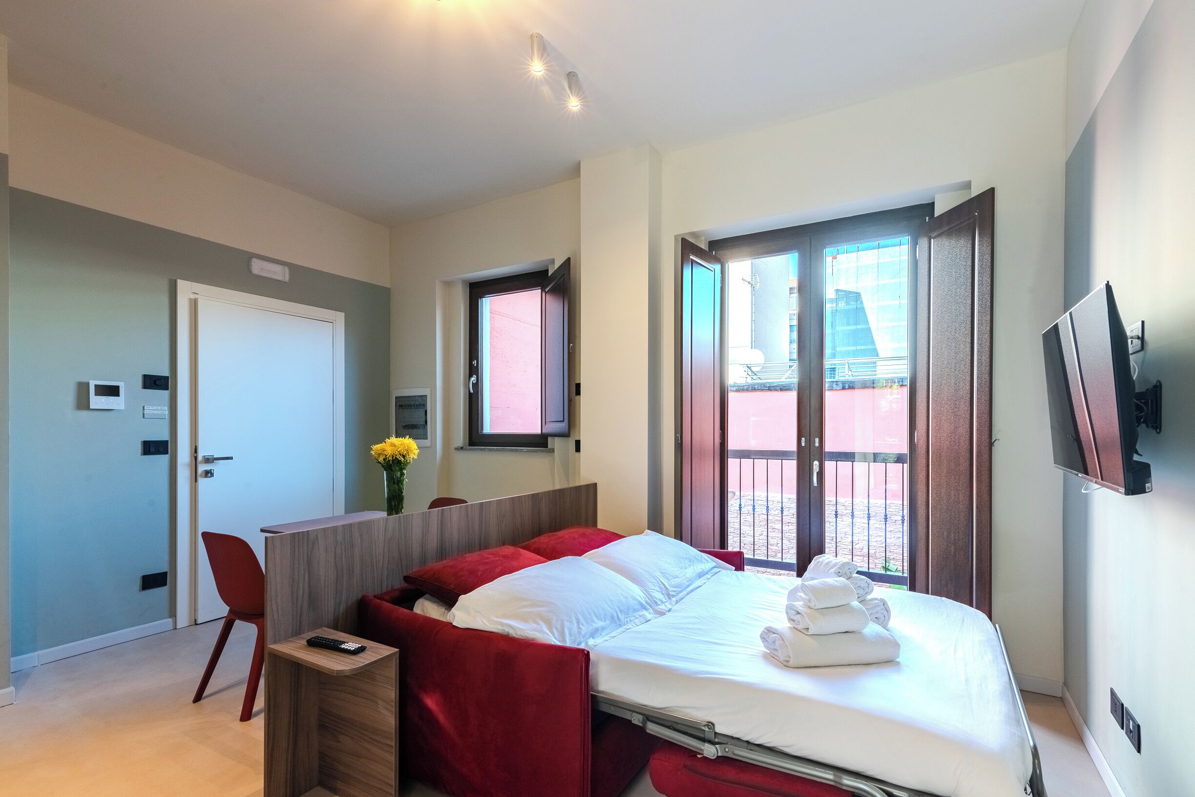 Una moderna camera d'albergo con un letto grande, una scrivania, una sedia, una TV e un balcone con vista.