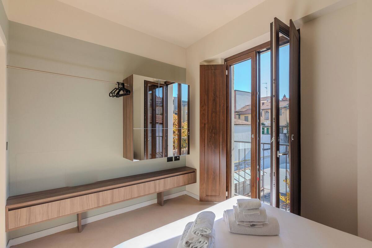 Un baño moderno con un banco de madera, un espejo grande y vistas al exterior mediante una puerta de cristal.