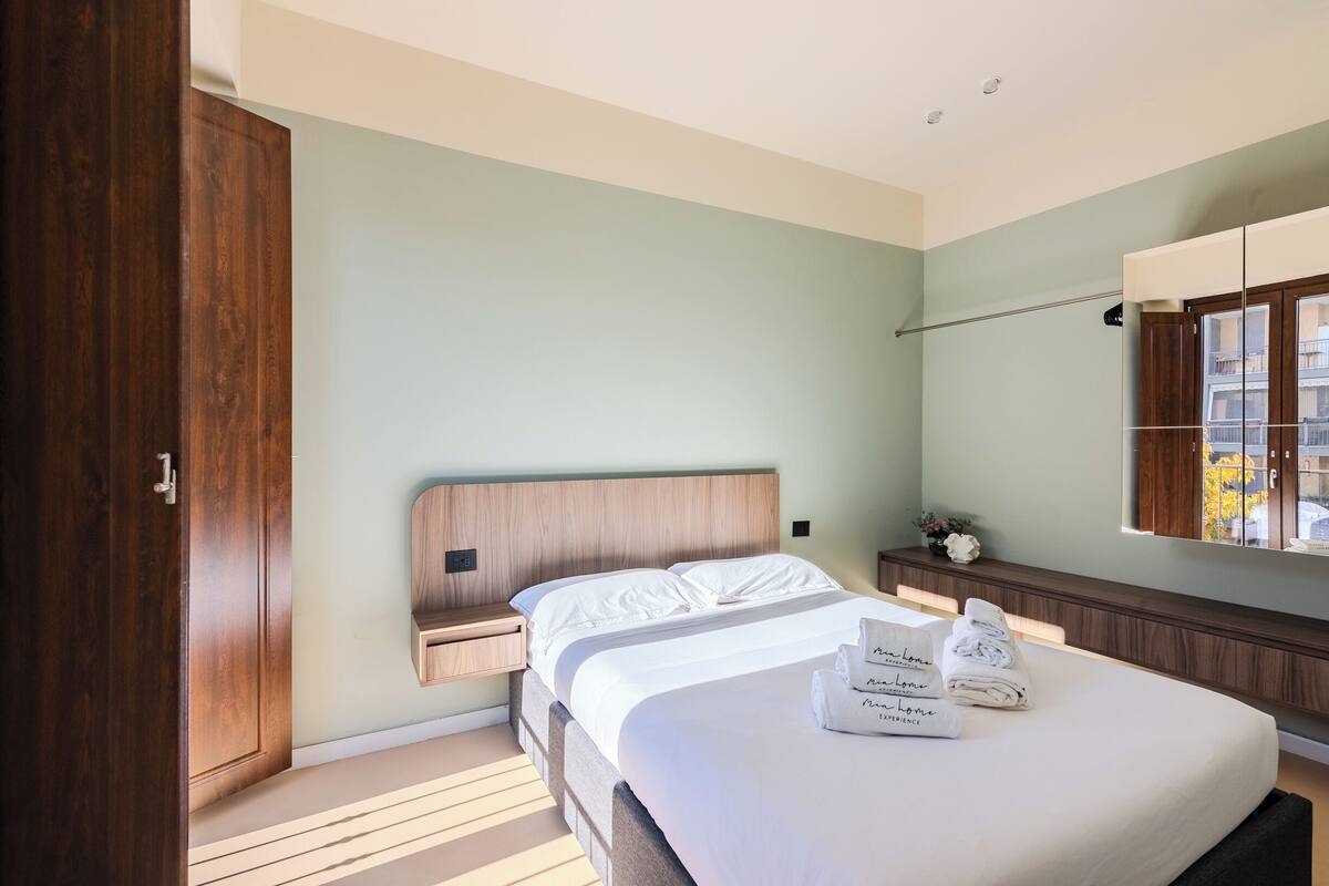 Una habitación de hotel con una cama grande, cabecero de madera, mesitas de noche y un espejo.