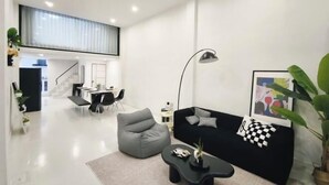 Un salon moderne avec un canapé noir, un fauteuil poire gris et une table basse noire. Un escalier mène à un niveau supérieur.