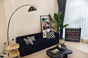 A living room with a black sofa, a round coffee table, a floor lamp, a framed picture, a plant, and a radiator. - FiveHouse Silom 1 Saladeang (Bangkok)