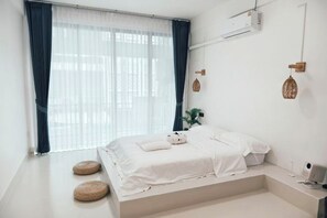 Een minimalistische slaapkamer met een bed, nachtkastje en een raam met gordijnen.