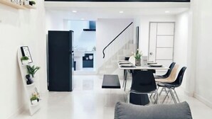 Un salon moderne et minimaliste, avec un canapé gris, un coin repas doté de chaises noires et un escalier menant à un niveau supérieur.
