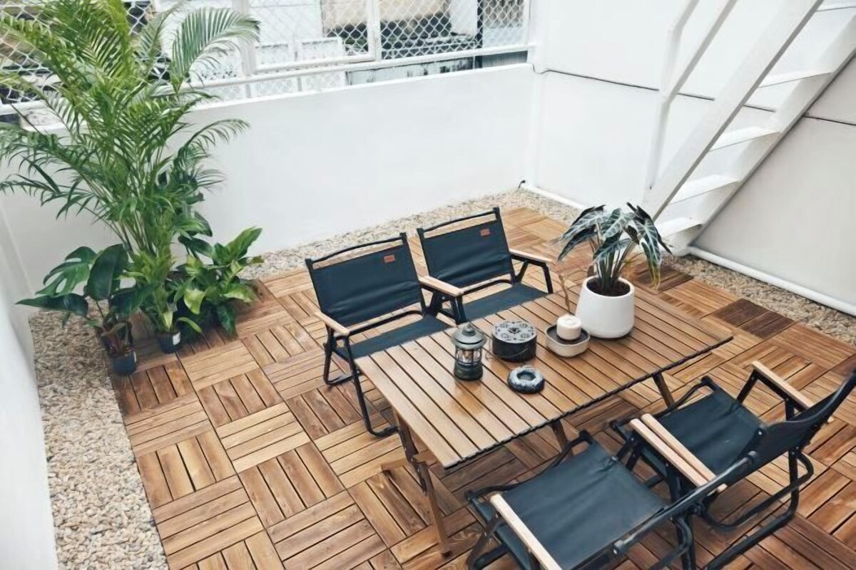 Een houten terras met een tafel en stoelen, omgeven door potplanten.