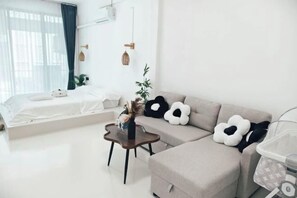 Een moderne woonkamer met een bank, een klein tafeltje, een bed en een ledikant.