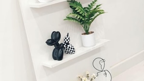 Une étagère blanche ornée d’objets décoratifs, notamment une plante en pot, un vase à carreaux et des sculptures abstraites.