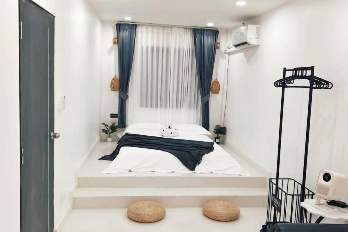 Ein Schlafzimmer mit einem Bett, einem Sessel, einem kleinen Tisch, einer Pendelleuchte und einem Fenster mit Vorhängen.