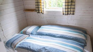 A small, single-bed room with a striped bedspread and matching pillows, a window with curtains, and wooden walls. - Blokhus with spectacular views in Jutland's nature area (Nørre Snede)