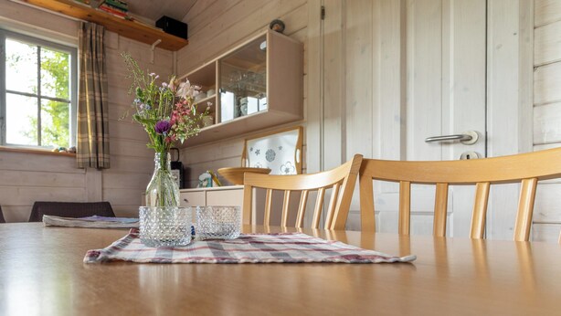 A wooden dining table with a vase of flowers, a glass, and a placemat. - Blokhus with spectacular views in Jutland's nature area (Nørre Snede)