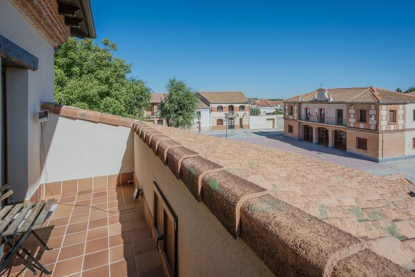A courtyard with a tiled floor, a balcony with a table and chairs, and buildings with traditional architecture in the background.