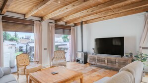 Un salon avec un plafond en bois, un téléviseur à écran plat, un canapé, un fauteuil et une table basse.
