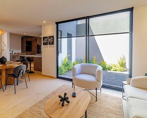 A modern living room with a large sliding glass door, a round coffee table, a sofa, and a chair.