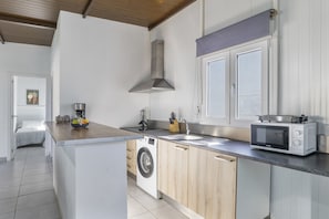 A compact kitchen with a washing machine, microwave, and wooden cabinets.