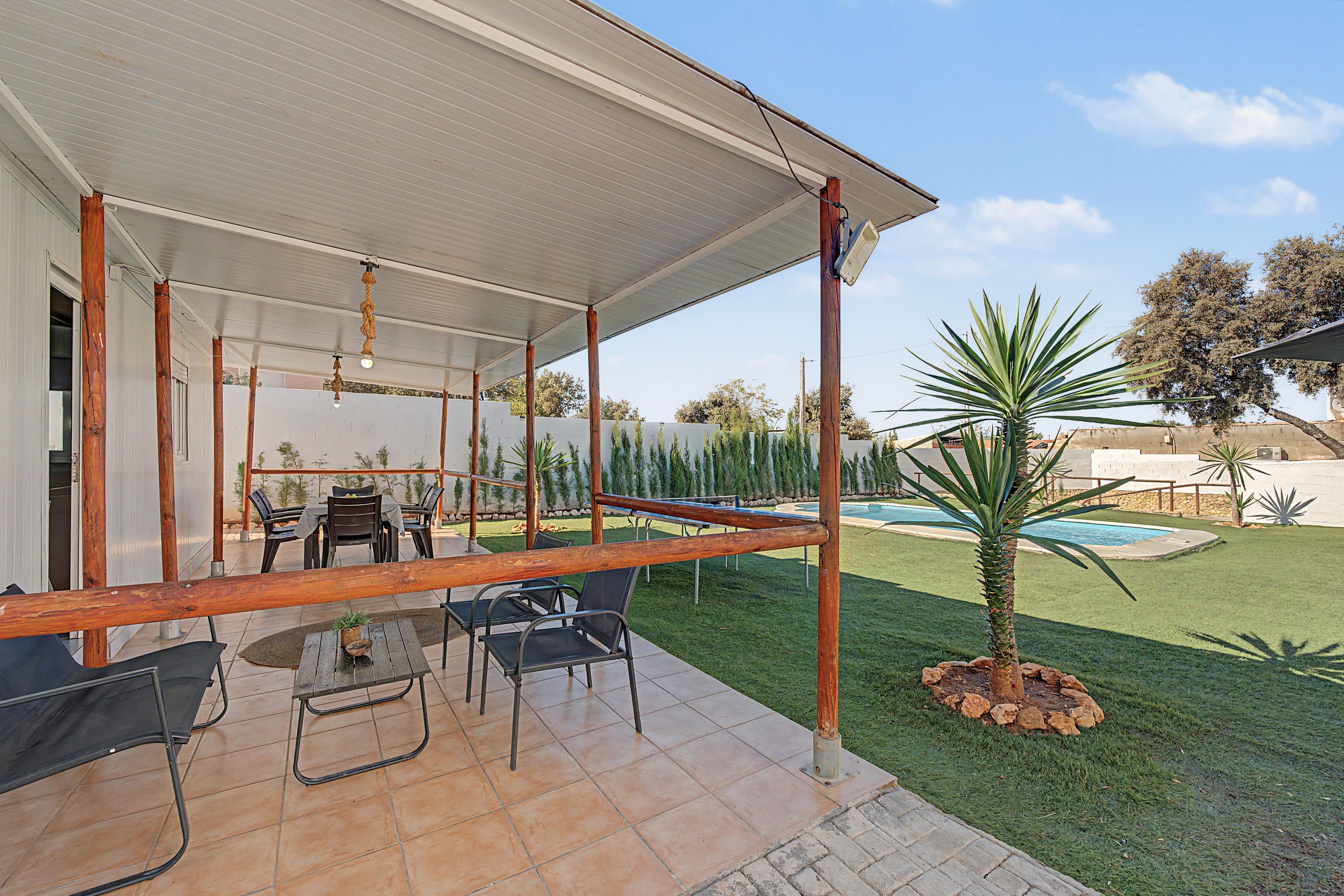 Un espacio al aire libre cubierto con piscina, mobiliario de patio y una pequeña palmera.