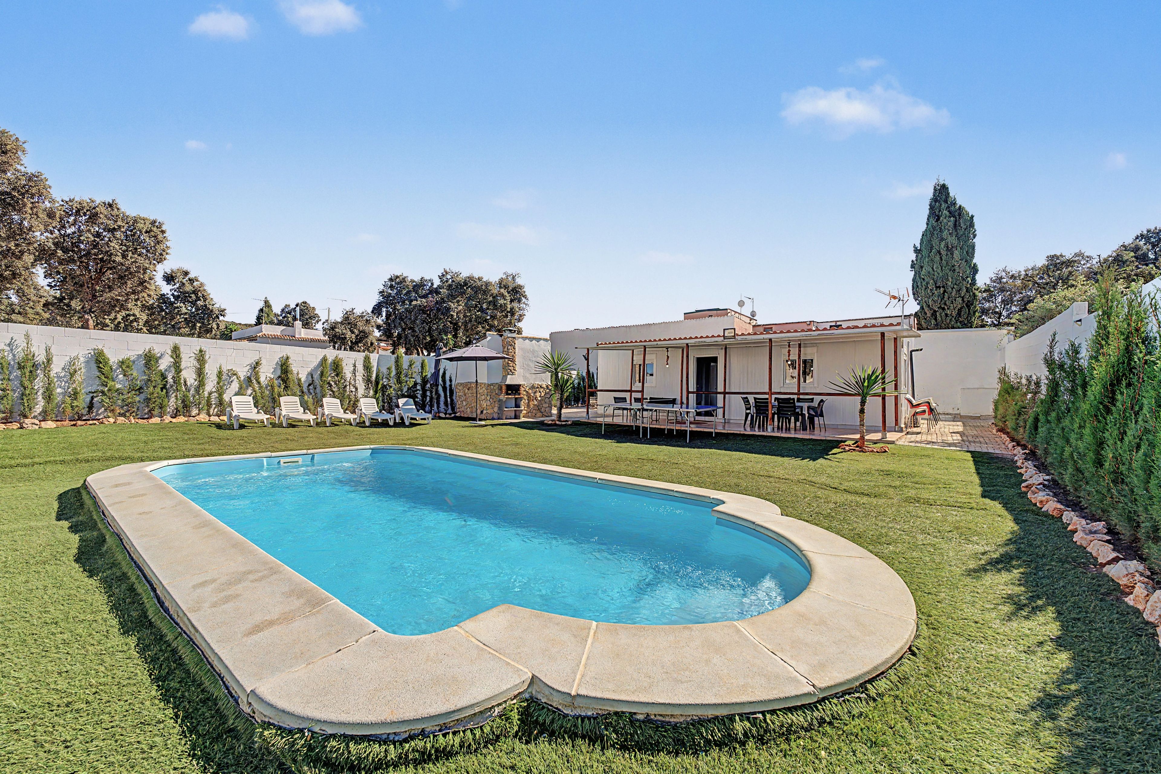 A swimming pool with a stone deck, surrounded by a well-maintained lawn and a patio area with outdoor furniture.