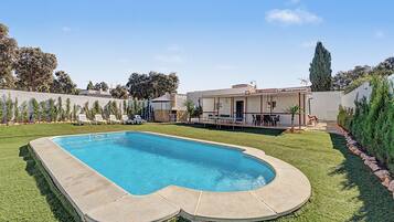 A swimming pool with a stone deck, surrounded by a well-maintained lawn and a patio area with outdoor furniture.
