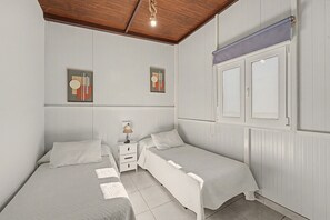 A bedroom with two single beds, a nightstand with a lamp, and a window with blinds. - Holiday Home 'El Encanto De Ronda' with Mountain View, Private Pool and Wi-Fi (Ronda)