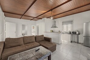 A modern living room with a brown sofa, a glass coffee table, and a kitchen area with white cabinetry and stainless steel appliances. - Holiday Home 'El Encanto De Ronda' with Mountain View, Private Pool and Wi-Fi (Ronda)