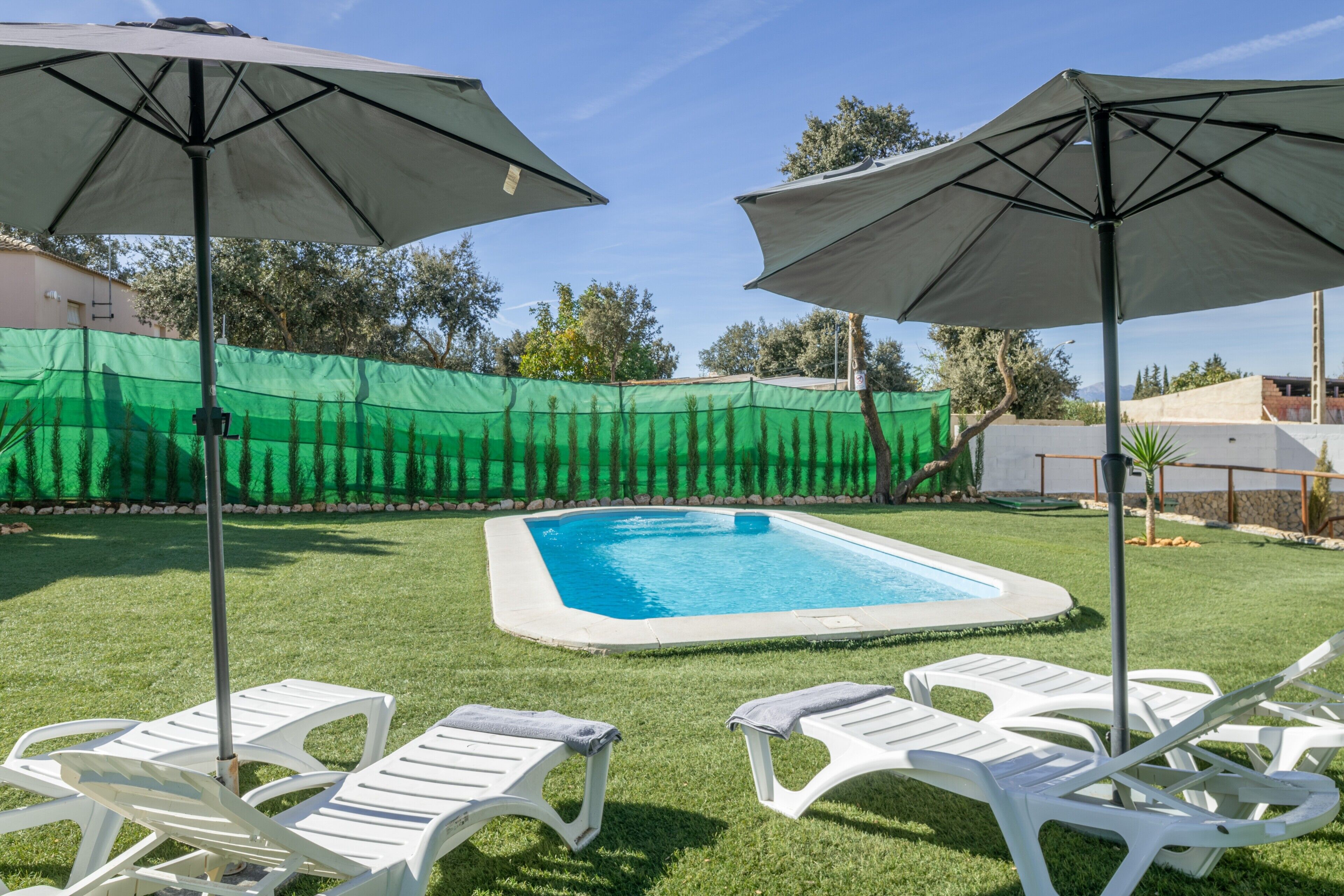Zwembad met witte ligbedden en parasols, omgeven door een groene omheining.