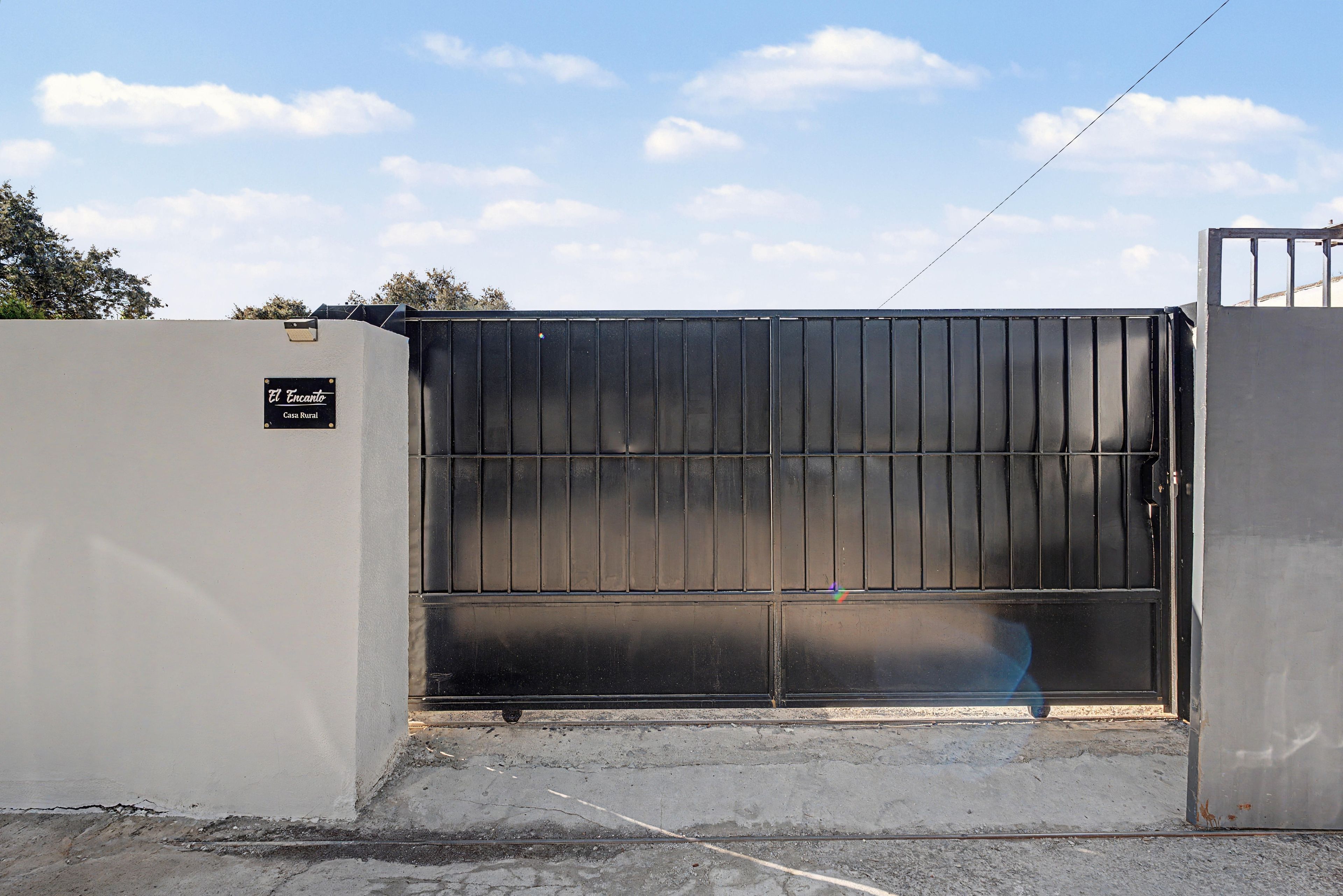A gated entrance with a metal gate and a sign that reads 'El Encanto Casa Rural.'