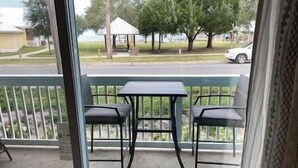 A balcony with a table and two chairs, overlooking a street with houses and a white car.