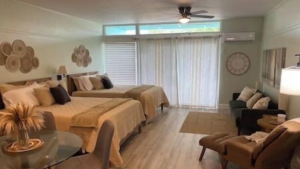 A hotel room with two beds, a sitting area with a table and chairs, a ceiling fan, and a large window with curtains.