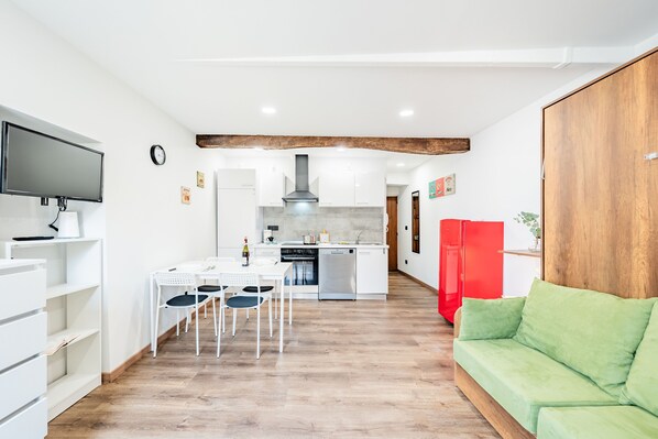 Une cuisine moderne avec des meubles blancs, un réfrigérateur rouge et un coin repas comprenant une table et des chaises blanches.