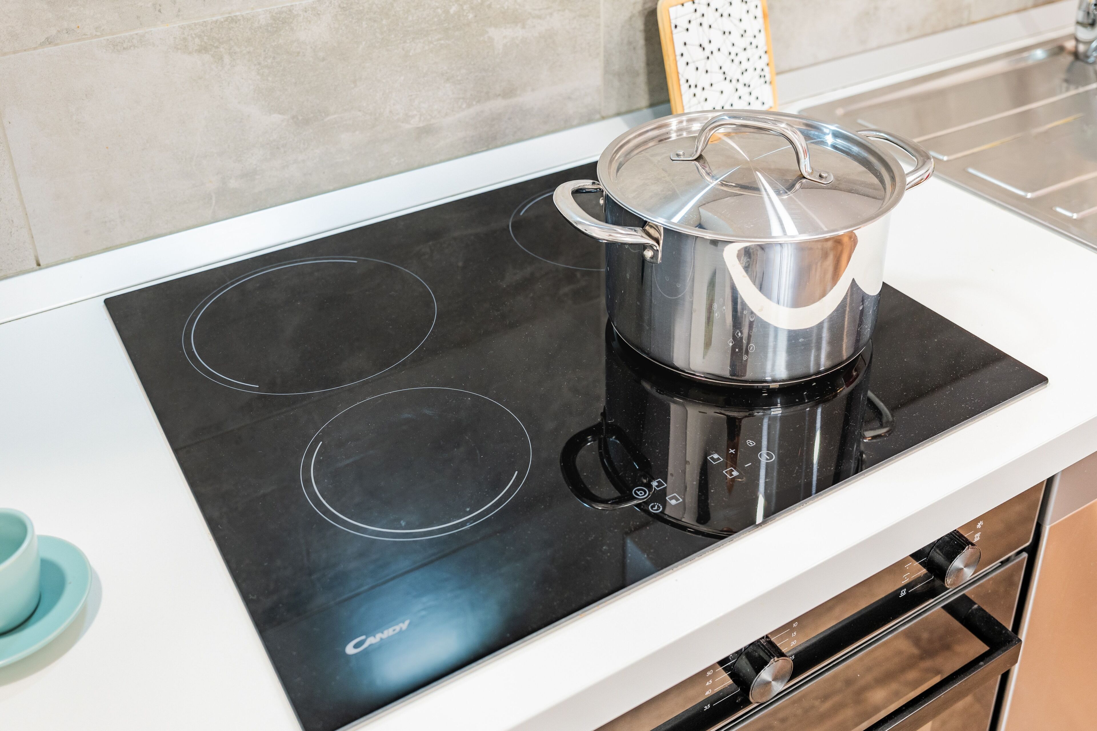 A modern kitchen with a black induction cooktop and a stainless steel pot on it.