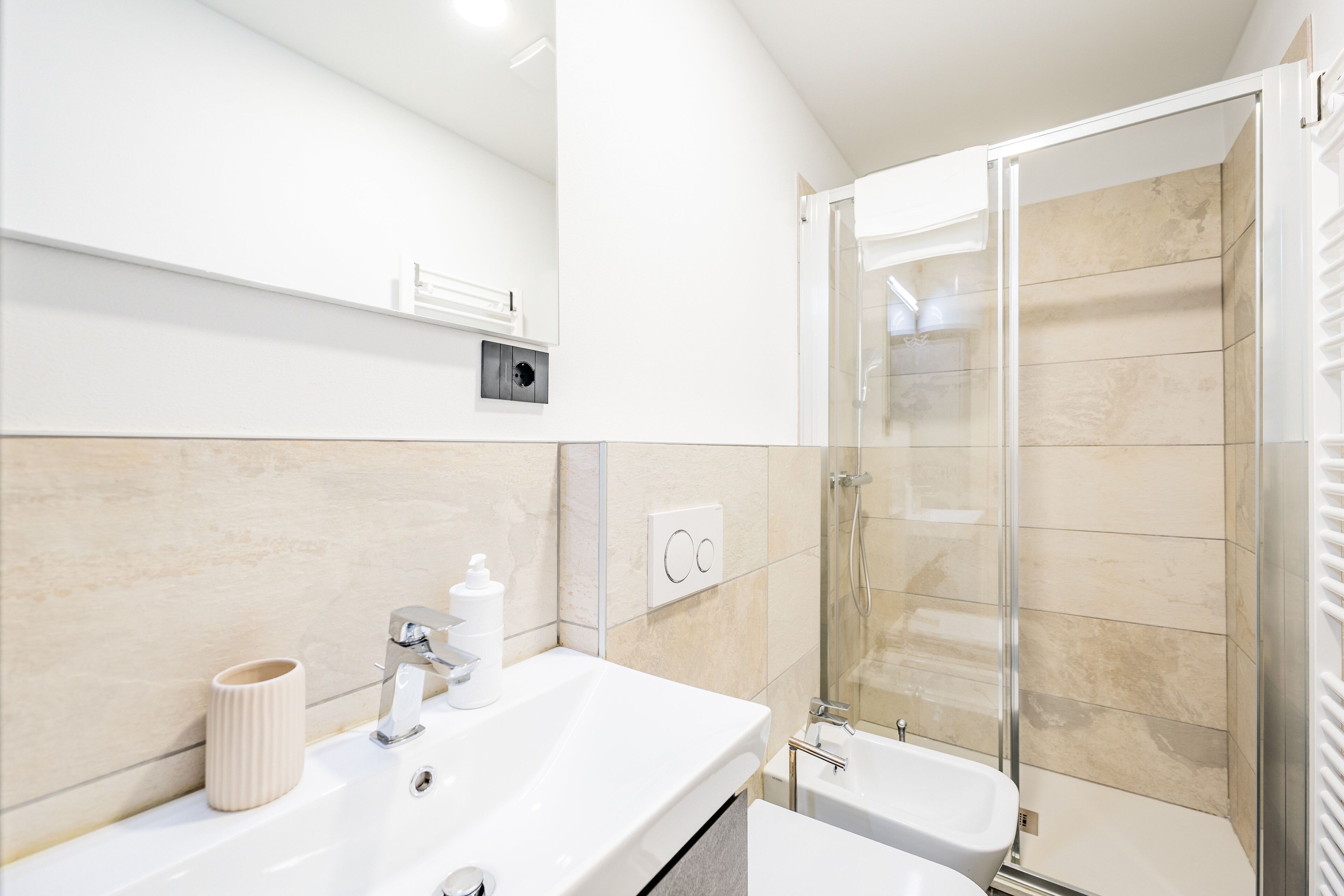 Ein modernes Badezimmer mit Waschbecken, Spiegel und einer Duschkabine aus Glas.