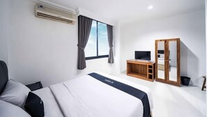 Quarto de hotel com cama, escrivaninha, guarda-roupa e janela com cortinas.