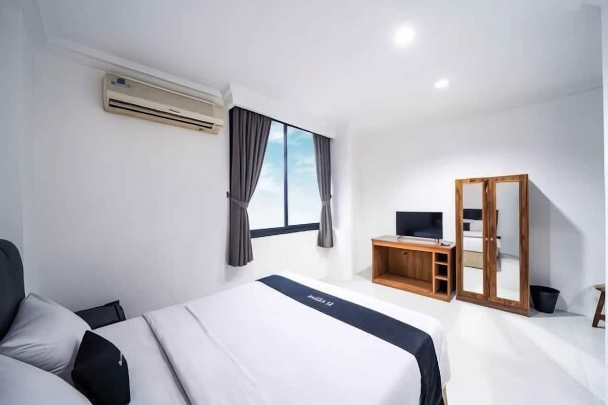 A hotel room with a bed, a desk, a wardrobe, and a window with curtains.