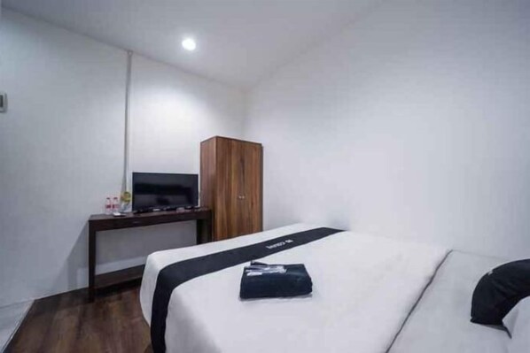 A hotel room with a bed, a wooden wardrobe, a desk with a television, and a small table with toiletries. - DS CoLive 34 Pecinan (Central Semarang)