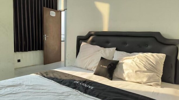 Uma cama com cabeceira preta, roupa de cama branca e preta, e um letreiro na parede.