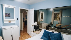 Une chambre à coucher comprenant un lit, une table de chevet, une commode, un miroir et une porte donnant sur une autre pièce.
