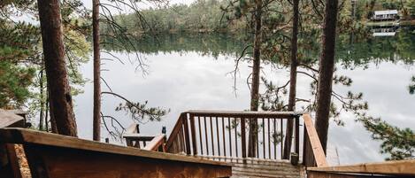 A wooden deck leading to a lake with trees surrounding it.