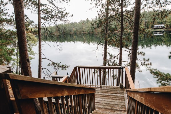 Une terrasse en bois qui mène à un lac, lequel est entouré d’arbres.