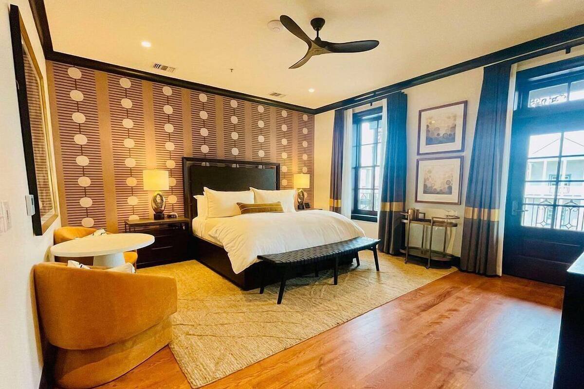 A modern hotel room with a large bed, a desk, a chair, and a balcony with curtains.