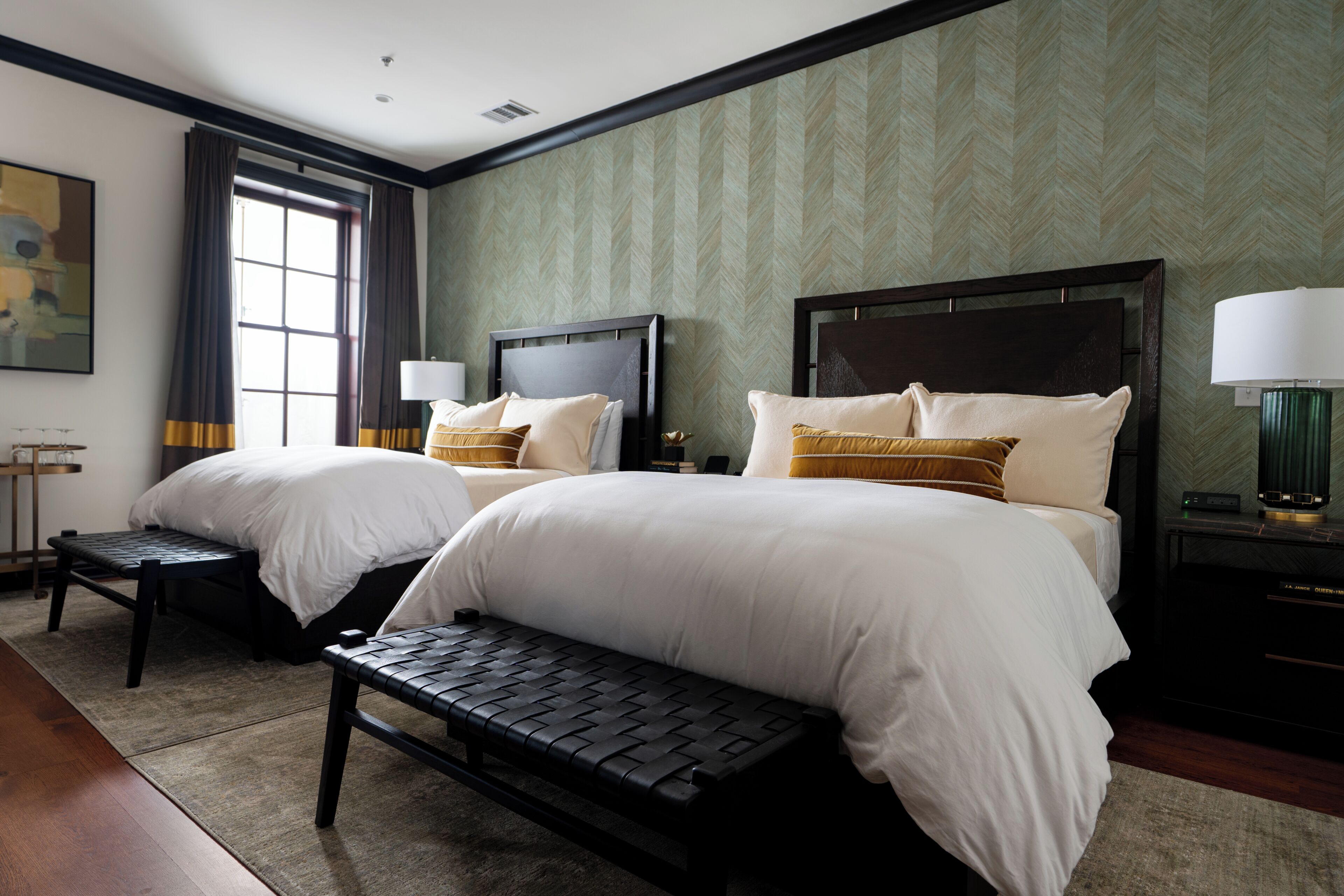 Une chambre d’hôtel avec deux lits, une banquette, une table de chevet avec une lampe et une fenêtre avec des rideaux.